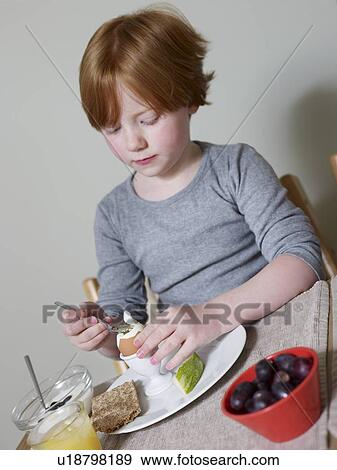 Stock Photo - 7-8 year old sits eating boiled egg. Fotosearch