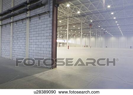 Stock Image - Access door to brightly lit and empty warehouse. Fotosearch