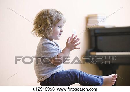 Stock Image - Blonde girl sits with paino clapping her hands. Fotosearch