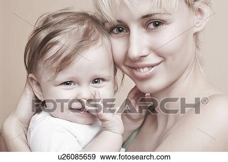Stock Photo - Blonde mother holds baby with hand in mouth. Fotosearch