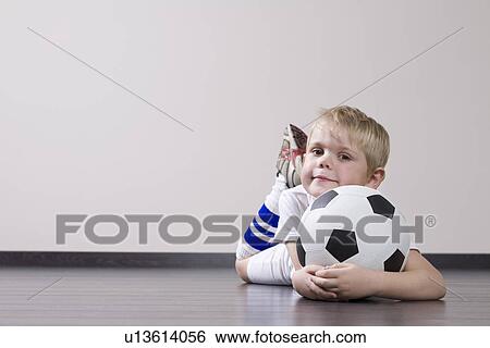 Stock Photograph - Boy lying on floor and holding soccer ball portrait. Fotosearch