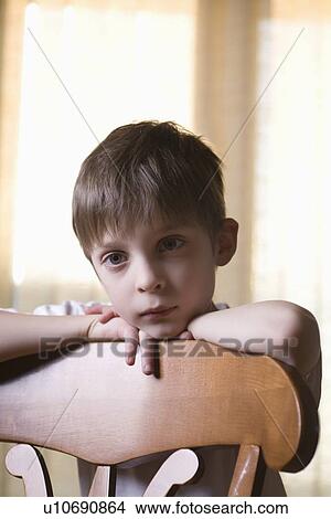 Picture - Boy sits looking at camera leaning on chair back. Fotosearch