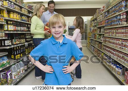 Picture - Boy stands with hands on hips with family shopping in supermarket. Fotosearch