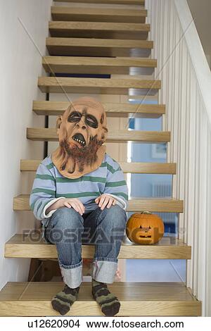 Boy wearing scary mask with pumpkin lantern on stairs View Large Photo Image Picture - Boy wearing scary mask with pumpkin lantern on stairs. Fotosearch