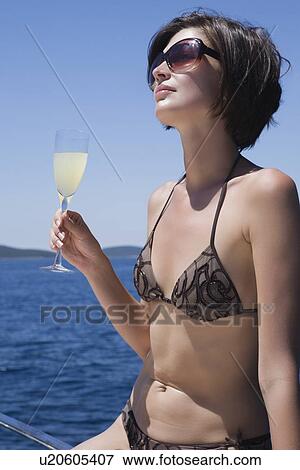 Stock Photo - Brunette woman sits on deck in bikini. Fotosearch