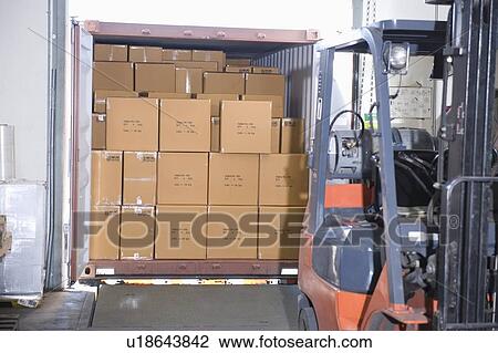 Stock Image - Cardboard boxes and fork lift truck in distribution warehouse. Fotosearch