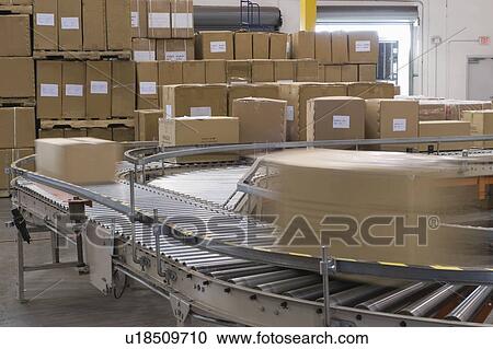 Stock Image - Cardboard boxes on conveyor belt in distribution warehouse. Fotosearch