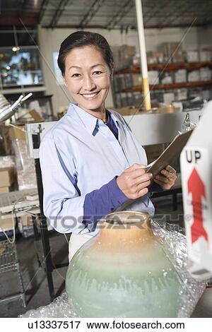 Stock Photo - Cheerful Asian woman working in distribution warehouse. Fotosearch