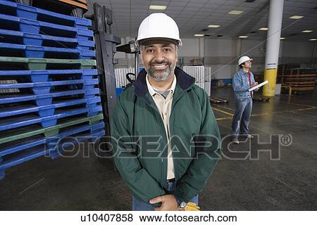 Cheerful man standing in factory wearing hart hat View Large Photo Image Stock Photo - Cheerful man standing in factory wearing hart hat. Fotosearch