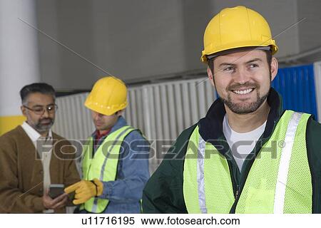Cheerful man standing in factory colleagues in background View Large Photo Image Stock Photography - Cheerful man standing in factory colleagues in background. Fotosearch