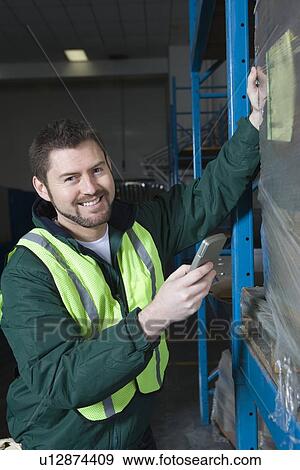 Stock Photo - Cheerful man using calculator in factory. Fotosearch