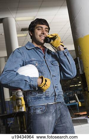Picture - Cheerful man using telephone in factory. Fotosearch