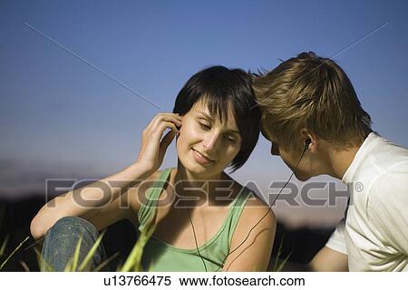 Stock Photography - Couple sit listening to music on shared earphones. Fotosearch