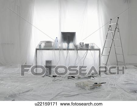 Stock Image - Desk and computer covered in transparent dust sheets in preparation for decoration. Fotosearch