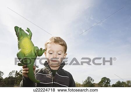 Stock Photo - Displeased boy holding toy dinosaur. Fotosearch