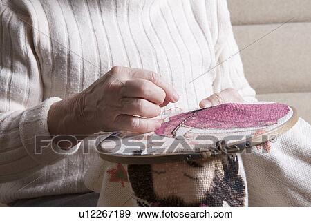 Stock Photo - Elderly woman sits working on needlepoint. Fotosearch