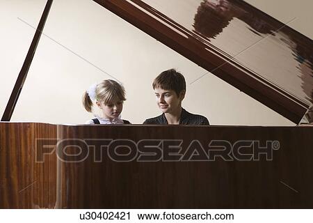 Stock Image - Female student (5-6) and teacher playing piano. Fotosearch