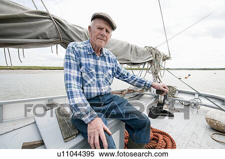 Stock Photography - Fisherman sits on deck of boat with mast and sail. Fotosearch