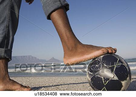 Stock Photo - Foot on soccer ball beach scene. Fotosearch