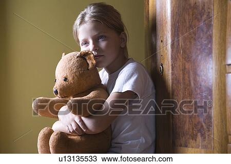 Stock Image - Girl embracing teddy bear in home. Fotosearch
