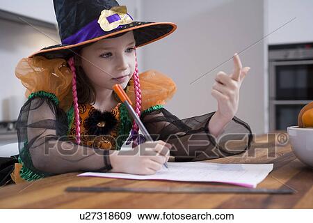 Stock Photo - Girl in witch costume drawing at table. Fotosearch