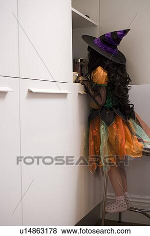 Stock Photo - Girl in witch costume looking in cupboard. Fotosearch