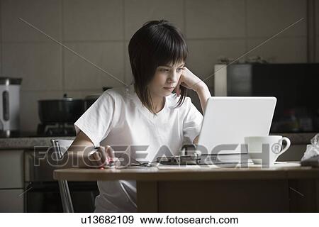 Stock Photo - Girl using laptop at kitchen table. Fotosearch