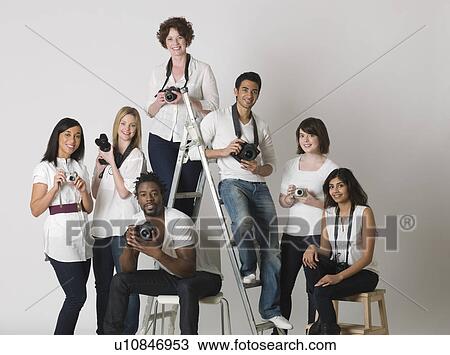 Stock Image - Group portrait of young photographers sitting on ladder and chairs. Fotosearch