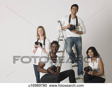 Stock Image - Group portrait of young photographers sitting on ladder and chairs. Fotosearch