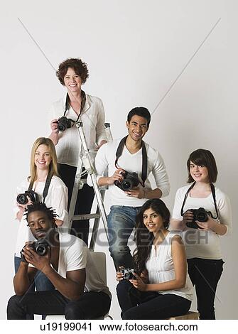 Stock Image - Group portrait of young photographers sitting on ladder and chairs. Fotosearch