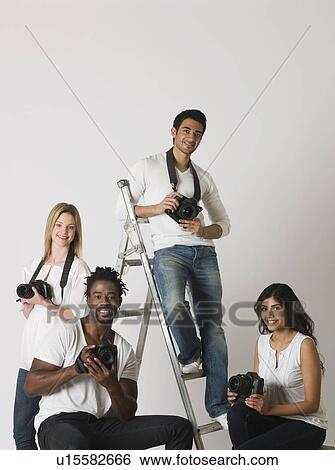 Stock Photograph - Group portrait of young photographers sitting on ladder and chairs. Fotosearch