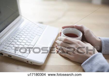 Hand holds a cup of black tea and laptop keyboard View Large Photo Image Picture - Hand holds a cup of black tea and laptop keyboard. Fotosearch