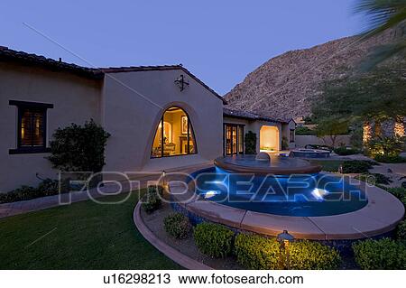 Stock Image - House exterior with fountain in garden at dusk. Fotosearch