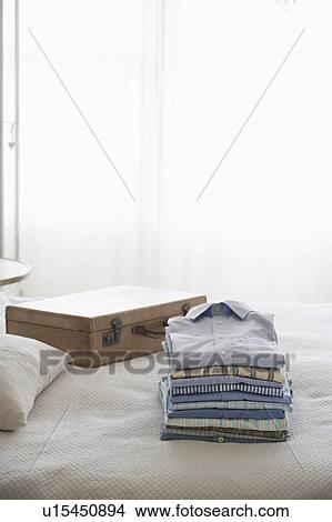 Picture - Ironed and folded shirts next to a suitcase. Fotosearch