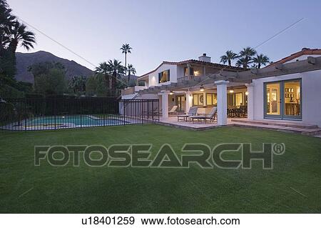Stock Photo - Lawn and swimming pool with lit exterior of Palm Springs home exterior. Fotosearch