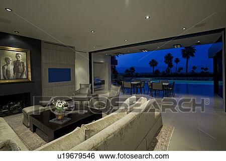 Stock Photograph - Luxurious interior with view of swimming pool and patio dusk. Fotosearch