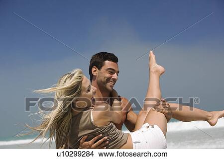 Picture - Man carrying woman on beach laughing. Fotosearch