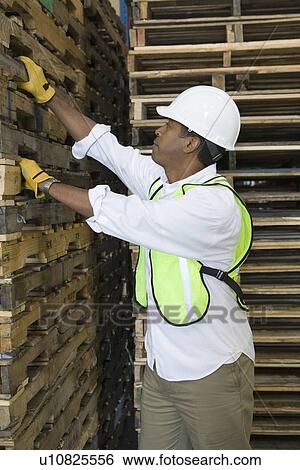 Stock Photograph - Man inspecting wooden pallets in distribution warehouse. Fotosearch
