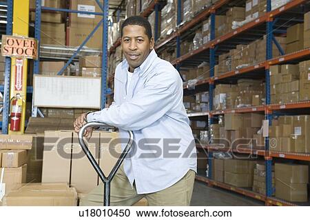Stock Image - Man leaning on trolley in distribution warehouse portrait. Fotosearch