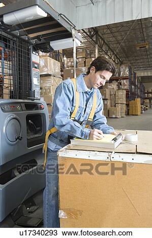 Stock Image - Man making notes in distribution warehouse. Fotosearch