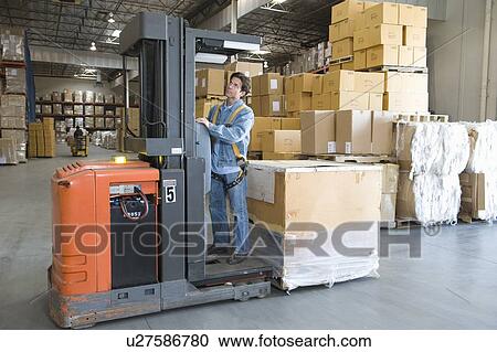 Stock Image - Man operating fork lift truck in distribution warehouse. Fotosearch