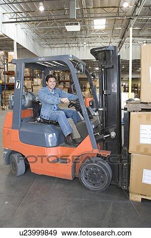 Stock Photo - Man operating fork lift truck in distribution warehouse. Fotosearch