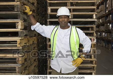 Stock Photo - Man standing near wooden pallets in distribution warehouse portrait. Fotosearch