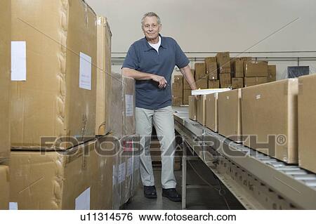 Stock Photograph - Man standing next to conveyor belt in distribution warehouse. Fotosearch