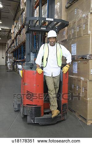 Stock Image - Man standing with fork lift truck in distribution warehouse. Fotosearch