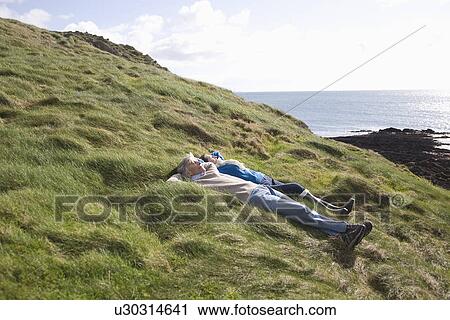 Mature couple lie with hands behind head in coastal landscape View Large Photo Image Stock Image - Mature couple lie with hands behind head in coastal landscape. Fotosearch