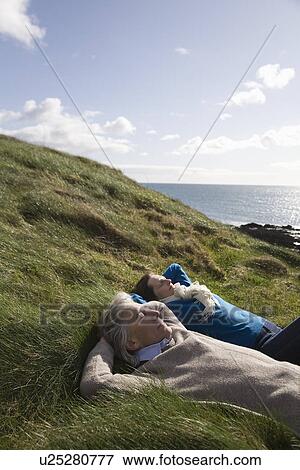 Mature couple lie with hands behind head in coastal landscape View Large Photo Image Stock Photo - Mature couple lie with hands behind head in coastal landscape. Fotosearch