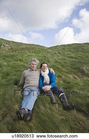 Stock Image - Mature couple sit full lengtgh on a hillside. Fotosearch
