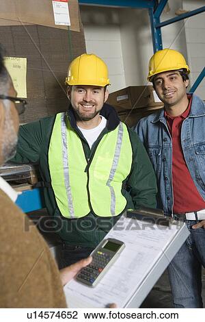 Stock Image - Men wearing hard hats in factory. Fotosearch