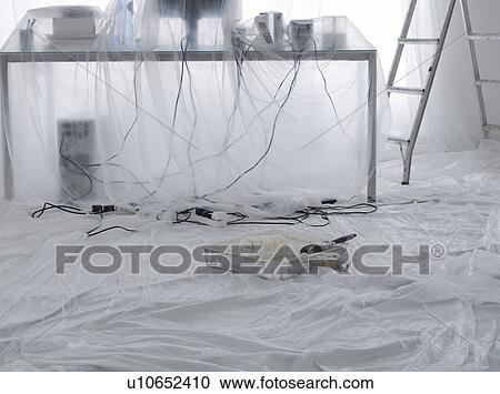 Stock Image - Messy desk with computer and cables covered in dust sheets. Fotosearch
